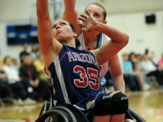 women's wheelchair basketball player shooting the basketball with an opponent attempting to block her.