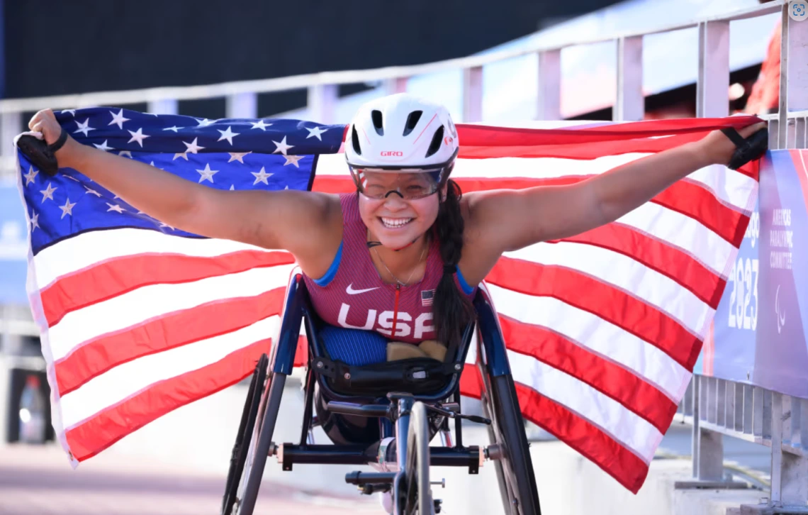 Photo of Paralympian Chelsea Stein racing and holding a US flag